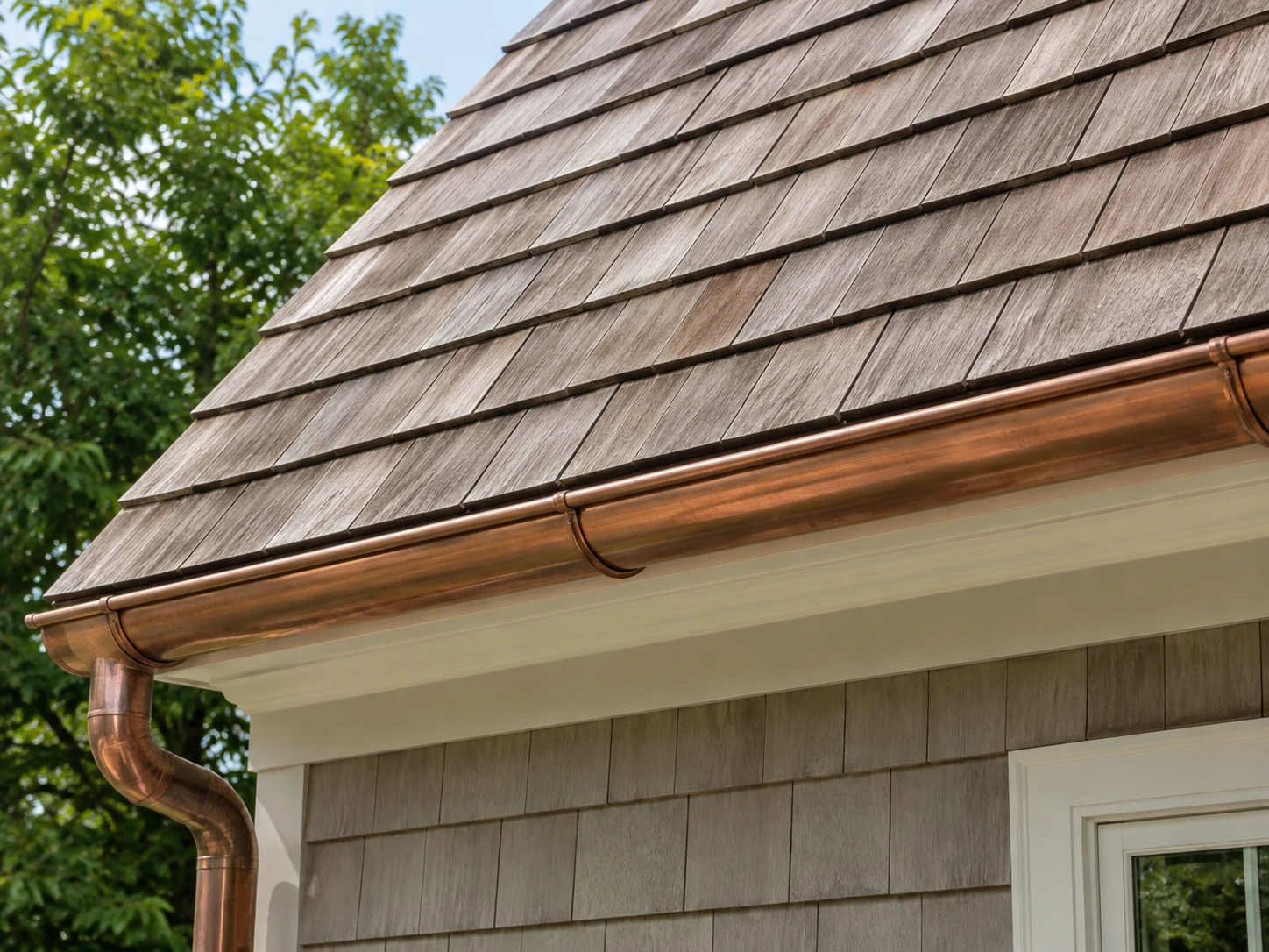 Weathered cedar roof shingles above a copper gutter, white fascia, and cedar shake siding.