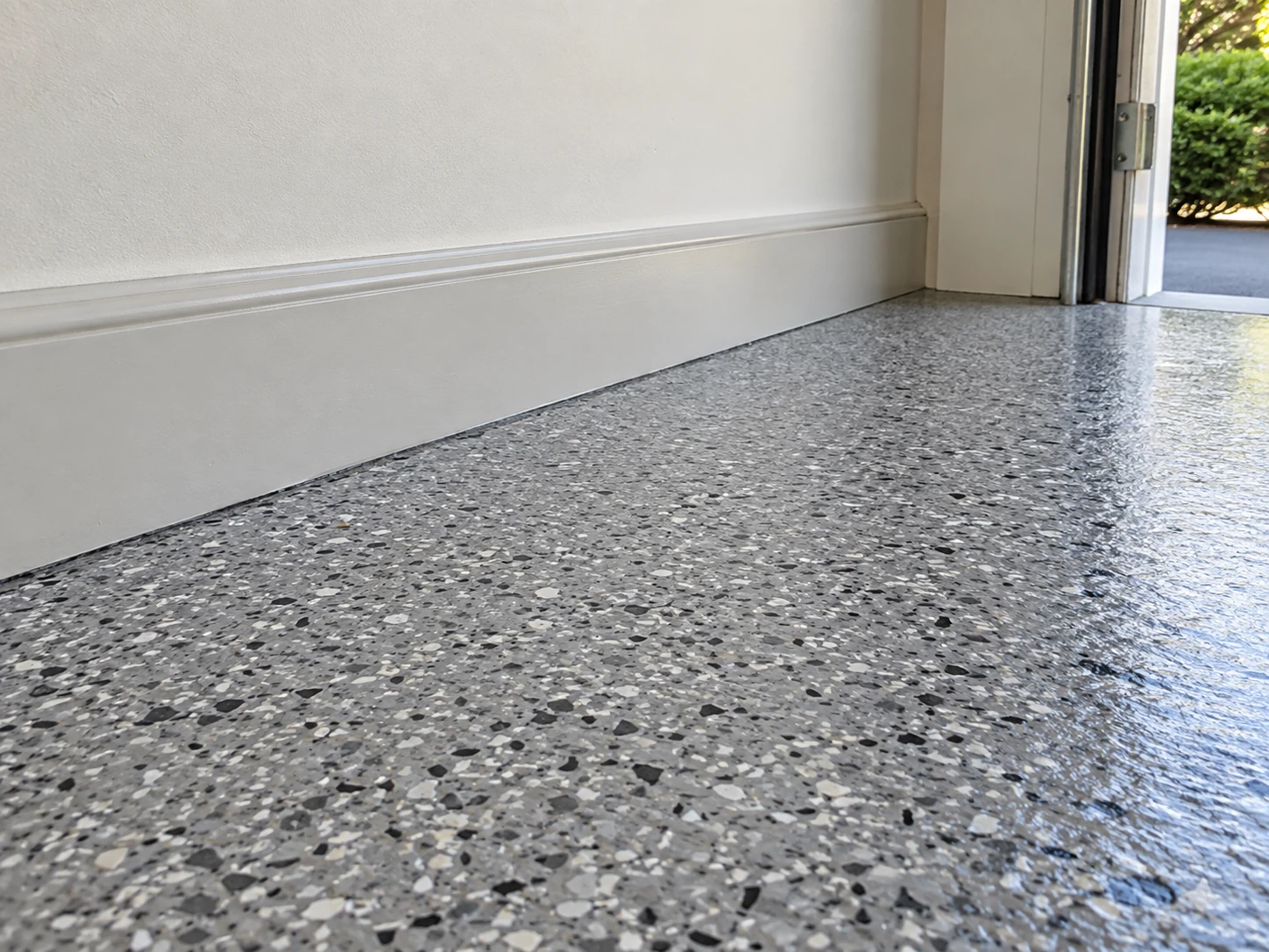 Gray flake epoxy garage floor coating along a white wall and open doorway.