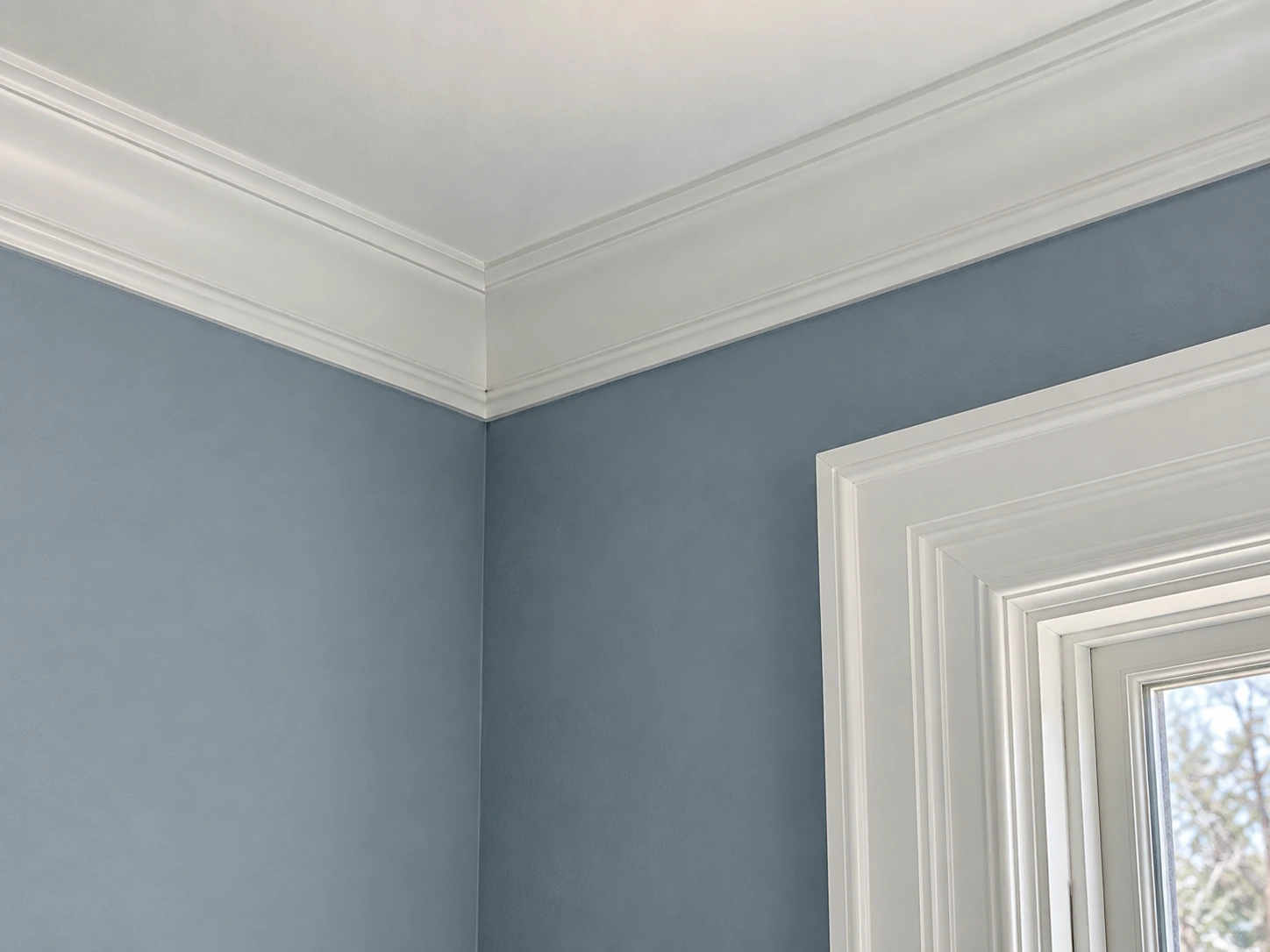 White crown molding and windowWhite crown molding and window casing against a soft blue painted wall.casing against a blue wall.