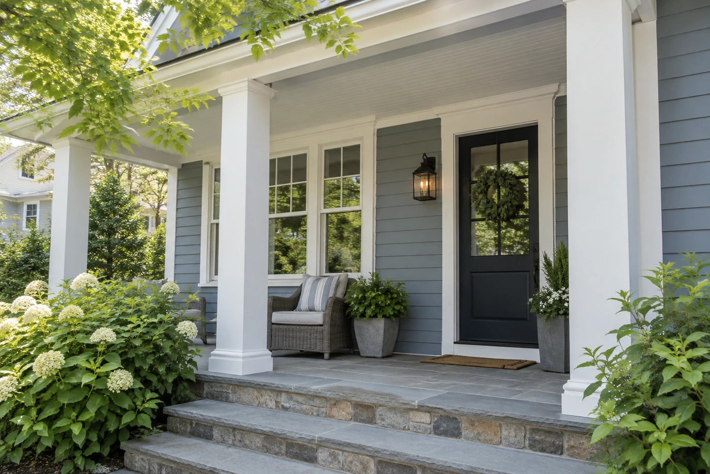 Blue-gray painted porch with white columns, white window trim, a dark front door, and stone steps.