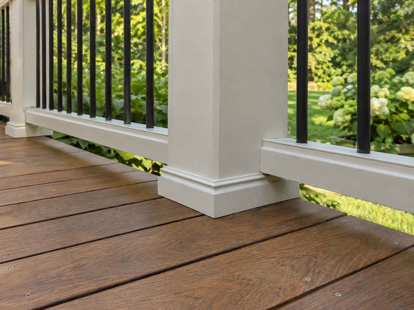 Brown stained deck boards around a white porch column with black metal balusters and white railing