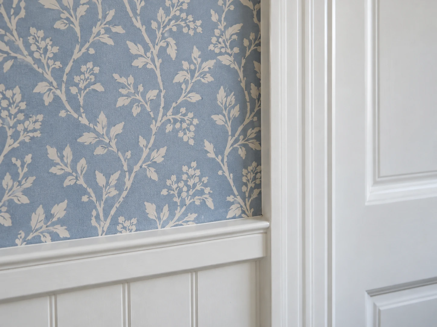 Blue botanical wallpaper meeting crisp white door casing and paneled wainscoting.